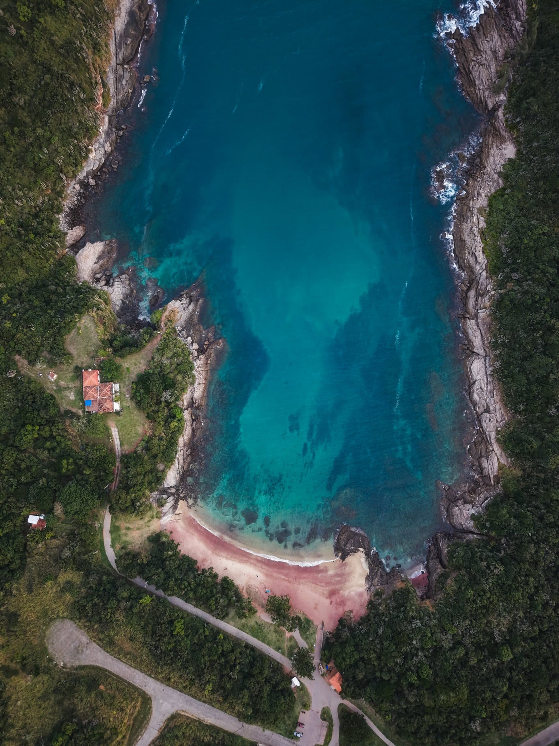 Top-down drone view of a deep turquoise cove ringed by forest and a small beach