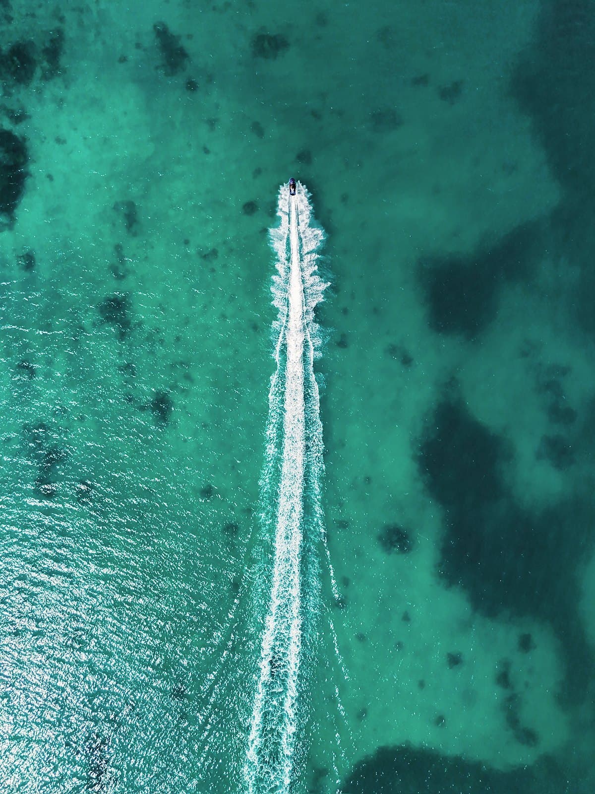 A single boat trailing a white wake over green reef water