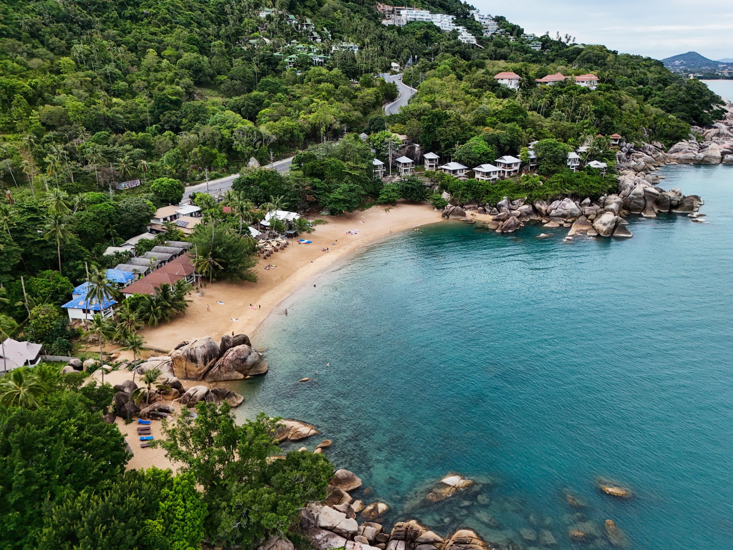 Aerial of a sandy cove with granite boulders, beach bungalows and clear water