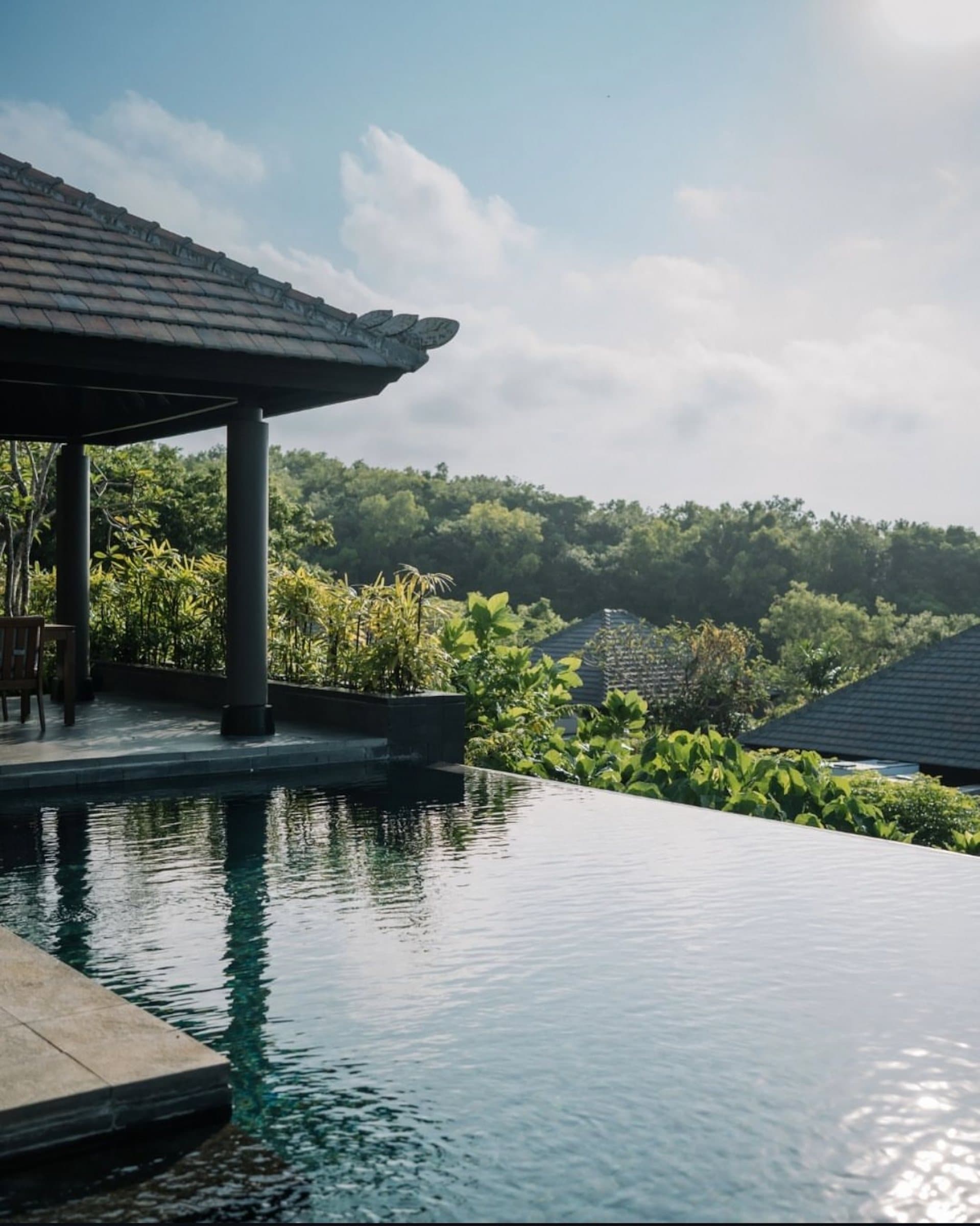 Infinity pool edge under a pavilion roof, jungle and cloud beyond