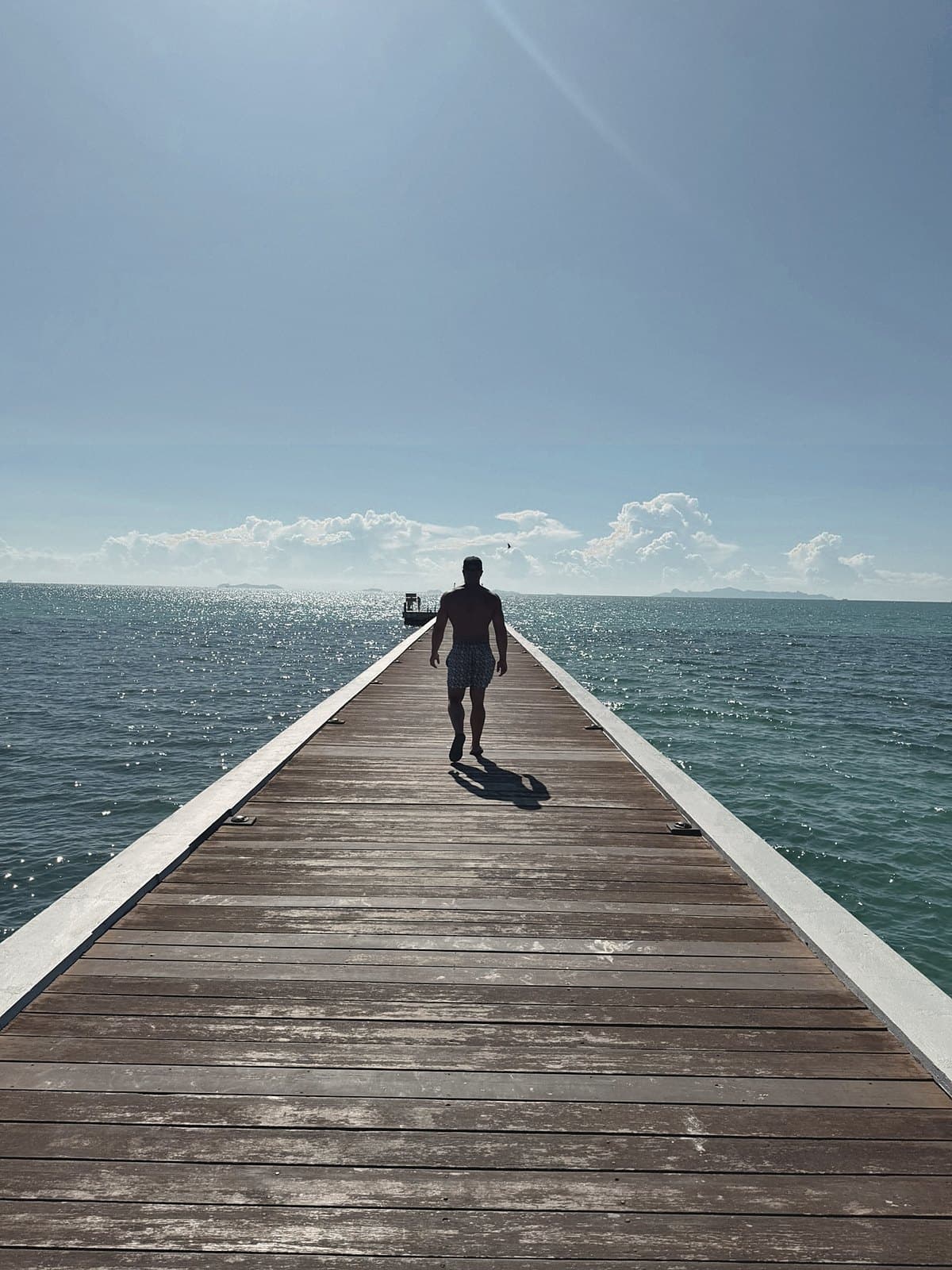 Figure walking down a long white pier over calm sea, back to camera