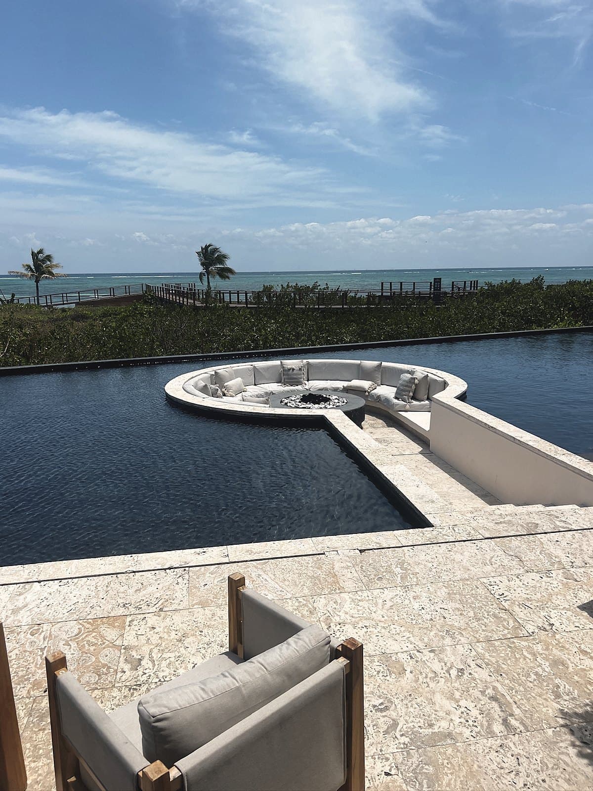 Sunken lounge in the middle of a dark reflecting pool, the sea behind and a chair in the foreground