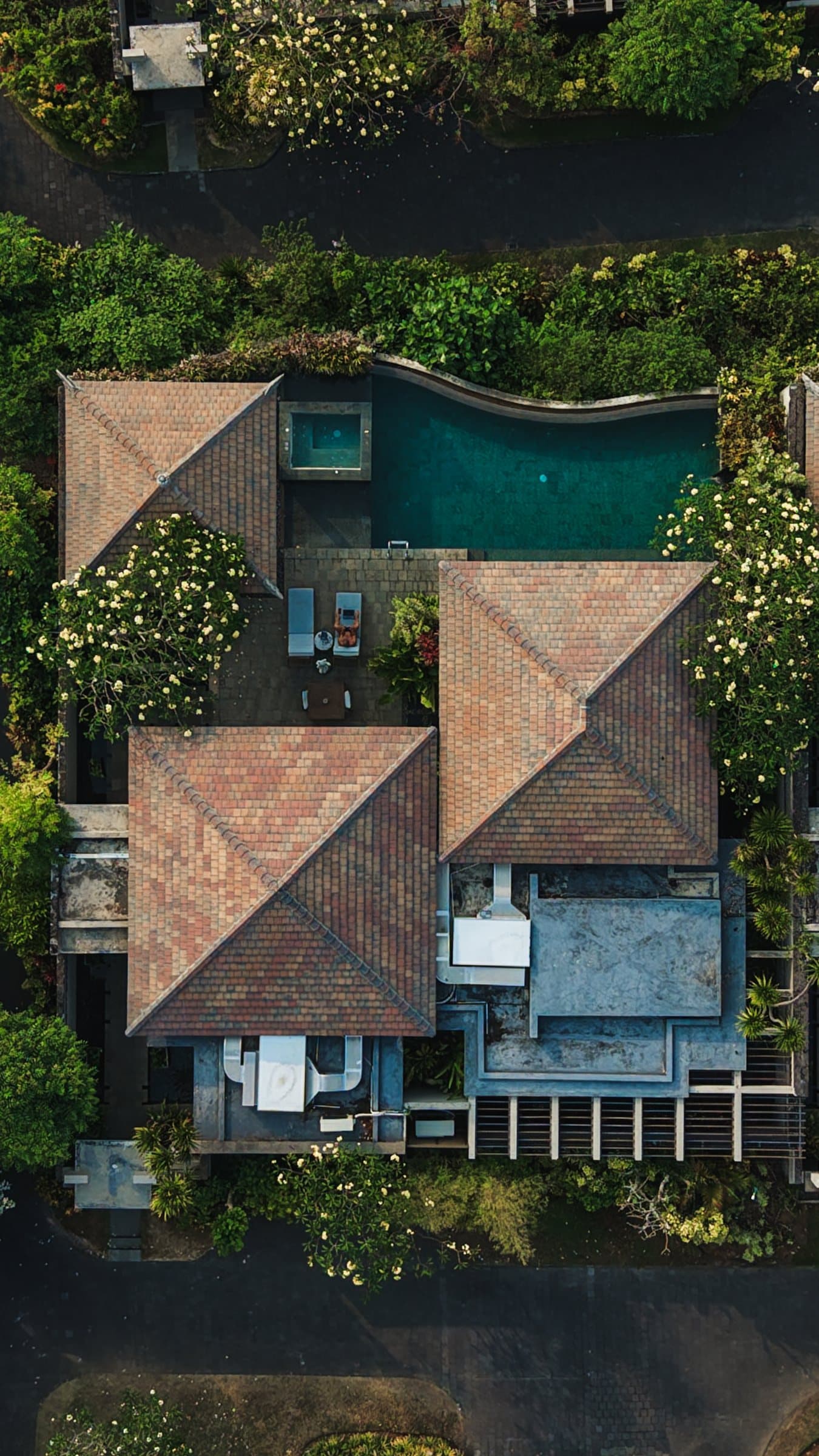 Top-down drone view of a villa with terracotta hip roofs and a green lap pool set in jungle